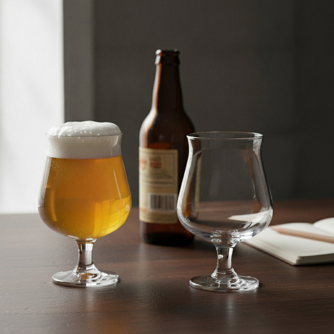 Belgian beer glasses with one filled with golden ale beside a beer bottle on a table