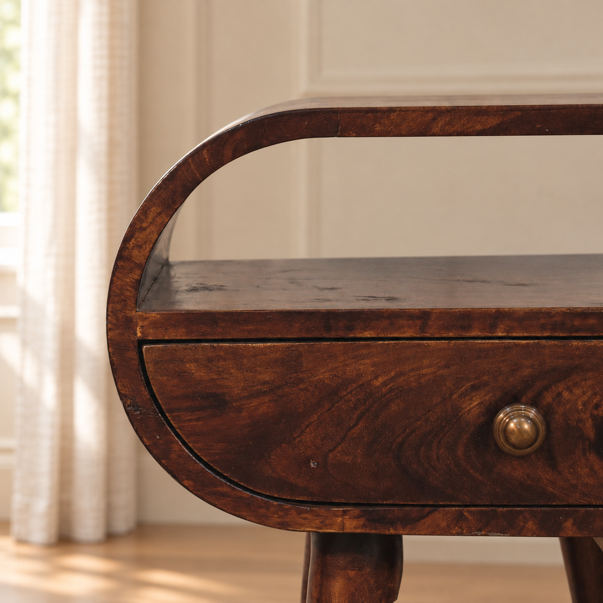 Close-up of the bedside table’s curved wooden frame, open shelf, natural wood grain and antique brass drawer knob.

