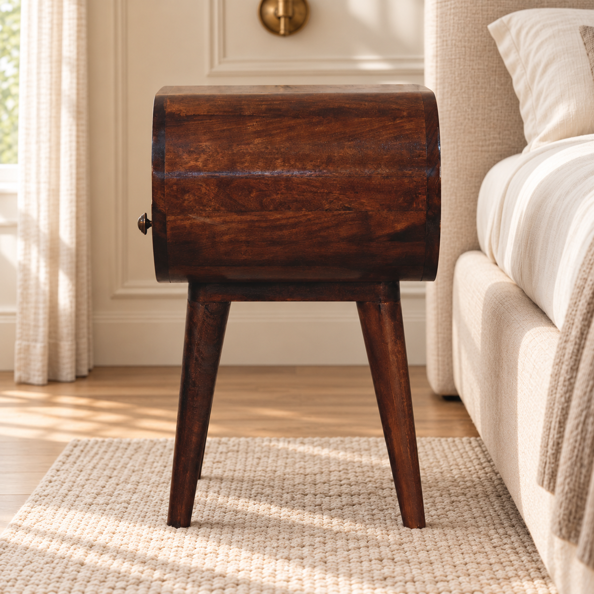 Side view of the walnut-finish bedside table showing its curved case, wood grain and tapered legs on an ivory rug.