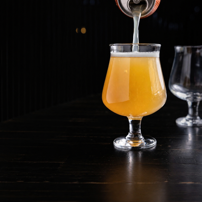 Golden craft beer being poured into a classic stemmed Belgian beer glass