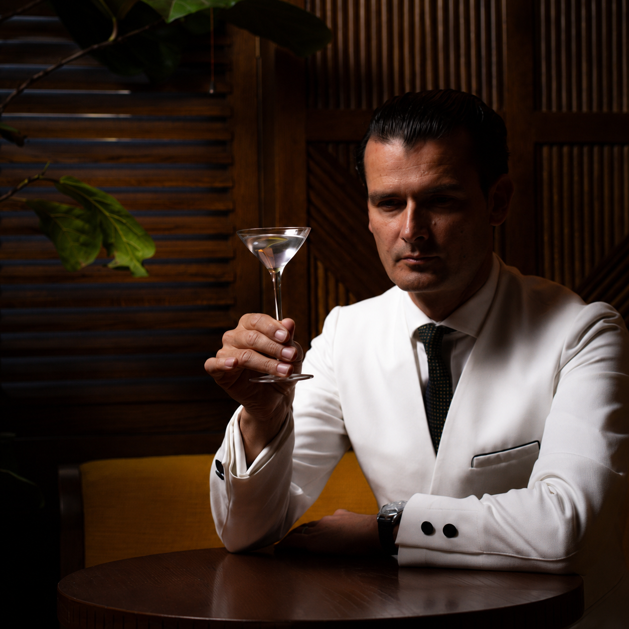 Man in white dinner jacket holding petite martini glass in classic bar