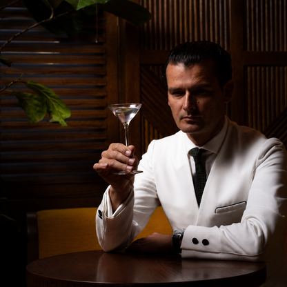 Man in white dinner jacket holding petite martini glass in classic bar