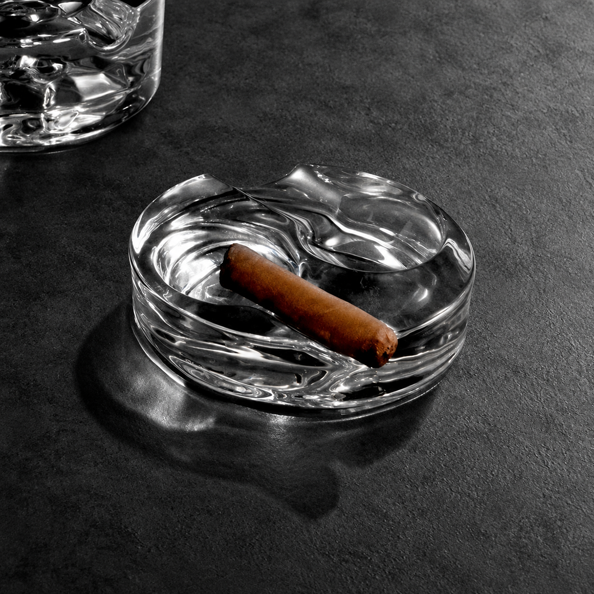 The Proper Cigar Bar crystal glass ashtray holding a cigar on a dark bar surface