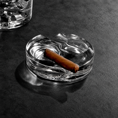 The Proper Cigar Bar crystal glass ashtray holding a cigar on a dark bar surface